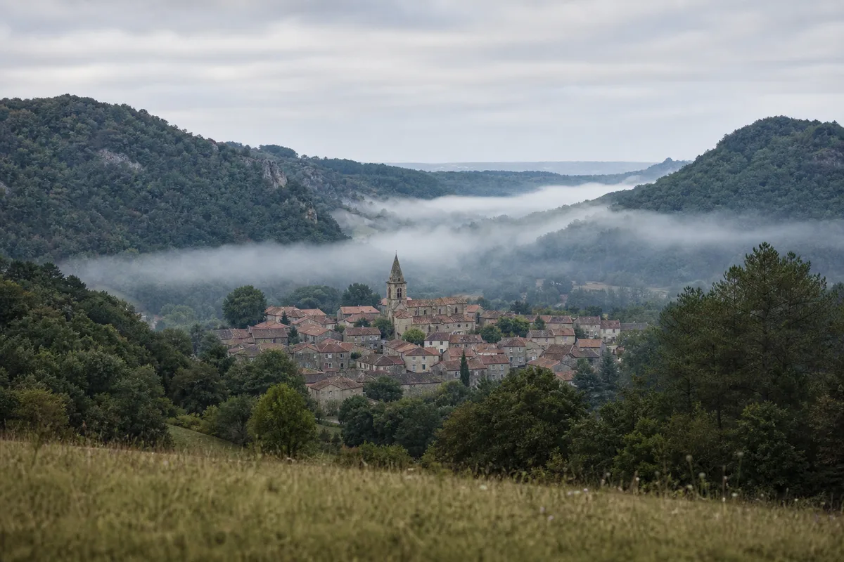 Village français avec clocher au fond d’une vallée boisée sous une brume légère