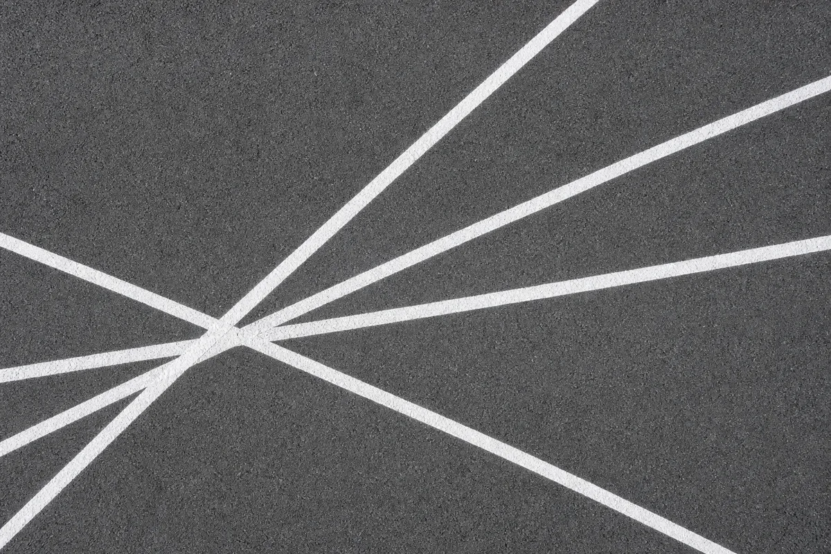 Lignes blanches peintes au sol se croisant en éventail sur un asphalte lisse, vue verticale