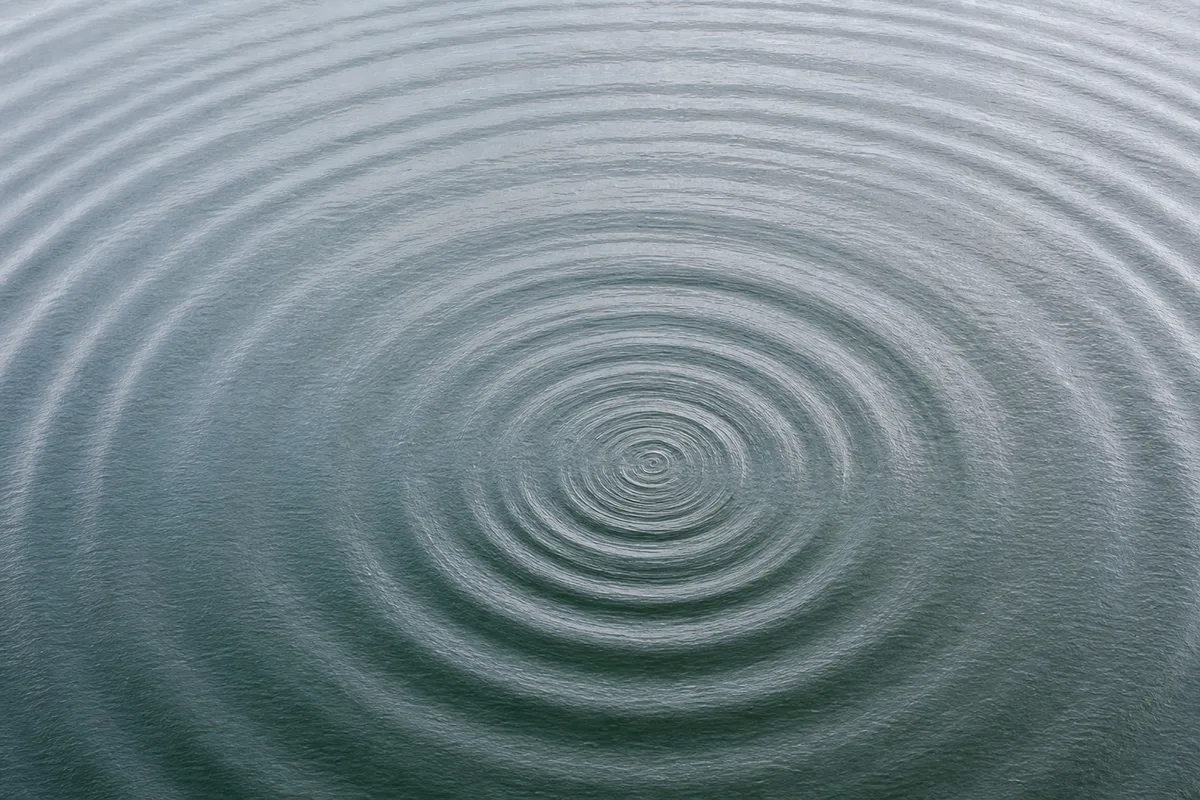Surface d&rsquo;eau calme parcourue de larges ondes concentriques, reflets gris argenté